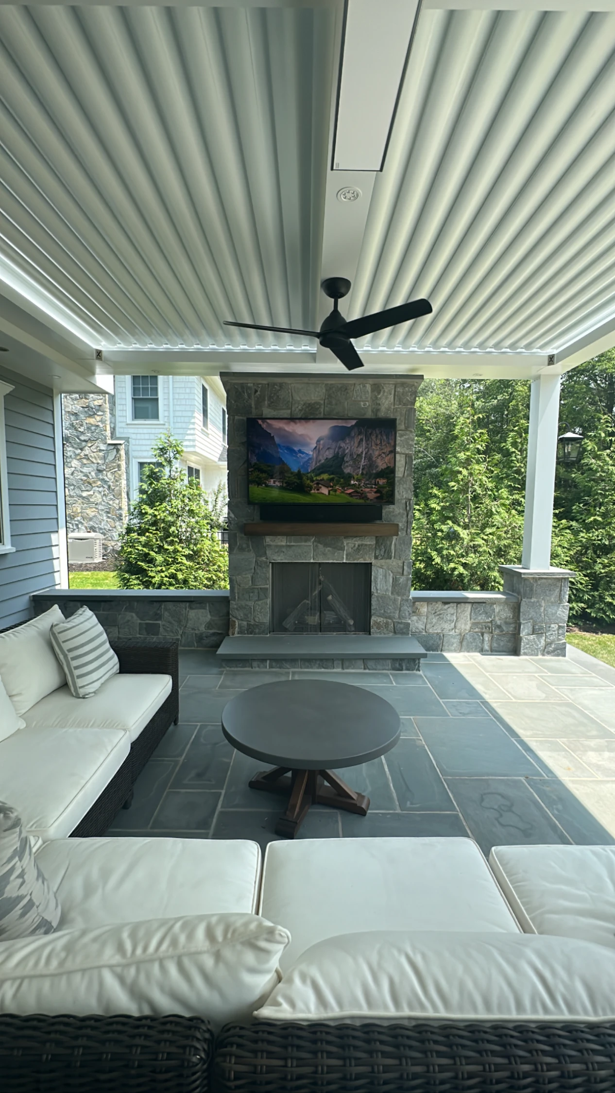 Outdoor TV mounted on stone fireplace under a covered patio