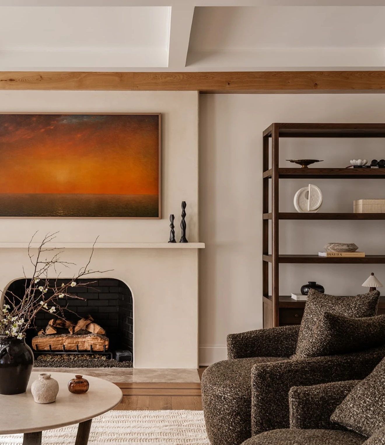 Frame TV above fireplace in a warm family room with wood beam and bookshelf